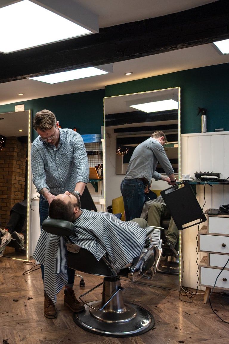 Barber cutting customers hair in a barbershop with teal walls and modern lighting