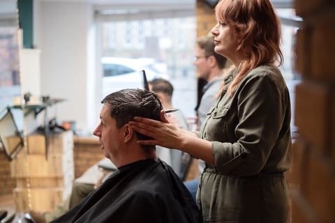 Hairstylist cutting a male clients hair in a salon with windows and city view